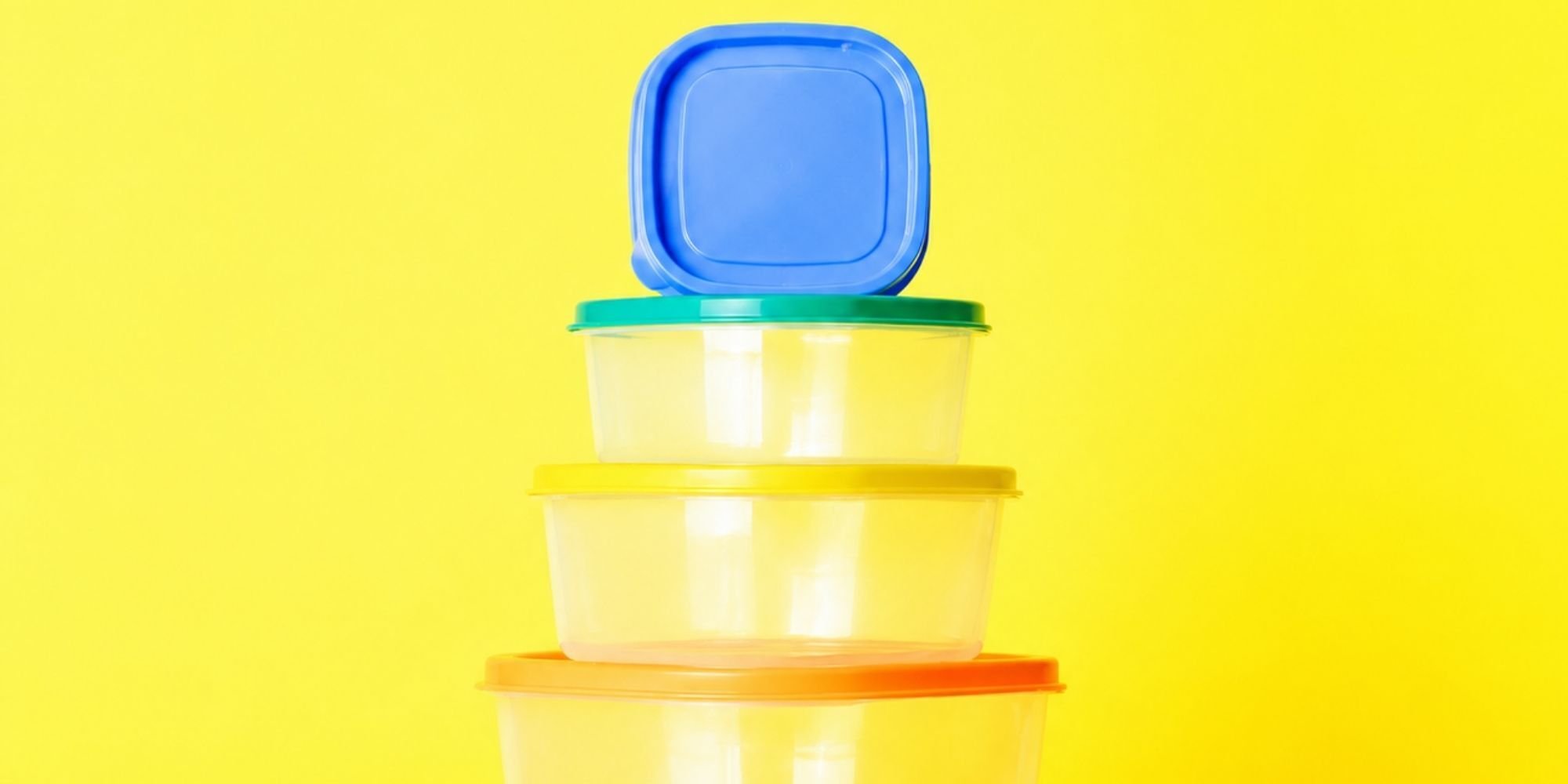 Gestapelde plastic opbergbakjes van polypropyleen met gekleurde deksels tegen een gele achtergrond