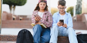 Twee tieners die buiten op hun smartphone kijken, ter illustratie van groepsdruk en FOMO bij jongeren