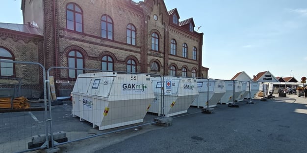Rij gelabelde afvalcontainers van GAKmiljö naast het historische Tullkammare-gebouw op een bouwlocatie in Zweden