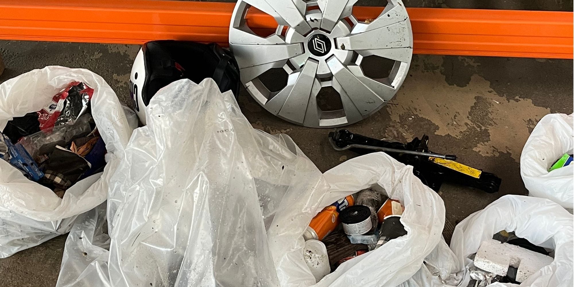 Milgro-collega's ruimen zwerfafval op met prikker en afvalzak tijdens World Cleanup Day, met een wieldop tussen het gevonden afval